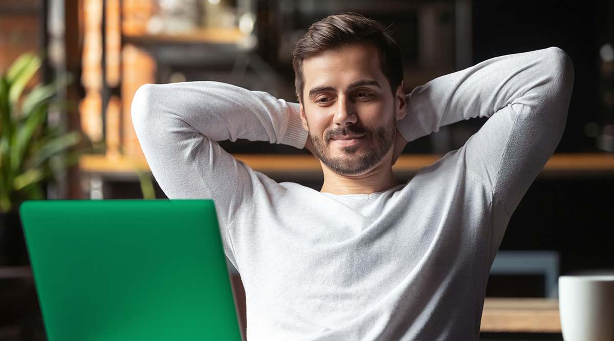 A man in a white sweater is sitting with his hands behind his head, smiling at the green glow of his laptop screen. Engrossed in the Survey 2022 results, he's relaxed in a cozy room with a blurred background and a hint of greenery peeking through on the side.