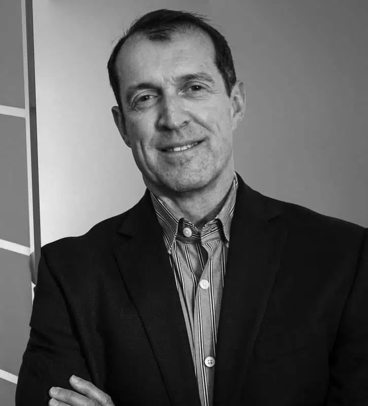 Black and white photo of a man in a suit, smiling with arms crossed, standing against a plain background.