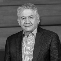 Older man in a suit and striped shirt, posing against a wooden background, black and white photo.