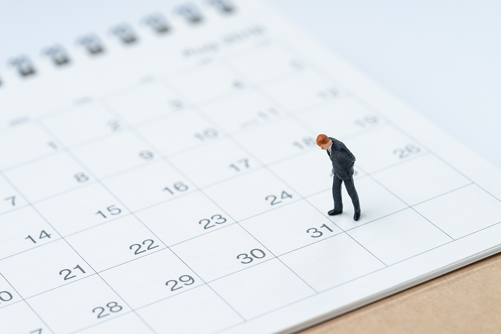 A small figurine of a man in a suit stands on a 2026 calendar page, pondering the true cost.